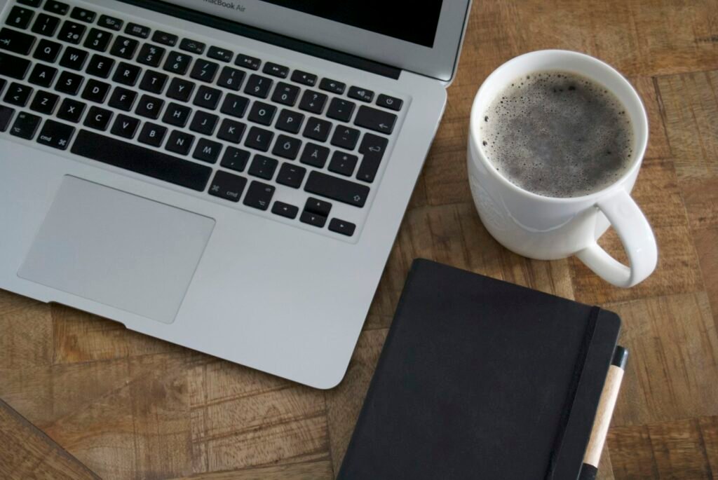 Ordinateur portable, mug de café et carnet noir posés sur un bureau en bois