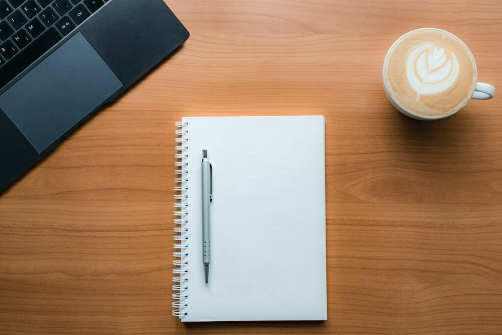 Carnet, stylo et café latte posés sur une table en bois à côté d'un ordinateur