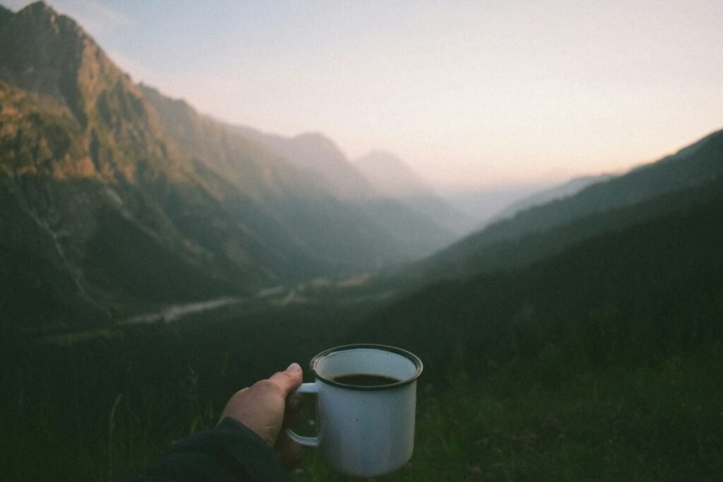Main tenant un mug de café face à une vallée de montagne au lever du jour